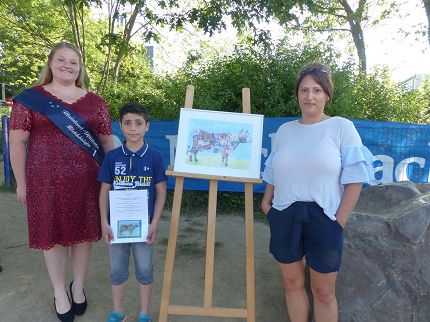 Milchkönigin Katharina freut sich mit Abdul (Klasse 4c) und Kunstlehrerin Frau Schmaus über den Gewinn. In der Mitte das Kunstwerk, das von der Jury aus über 1.500 Bildern gewählt wurde.
